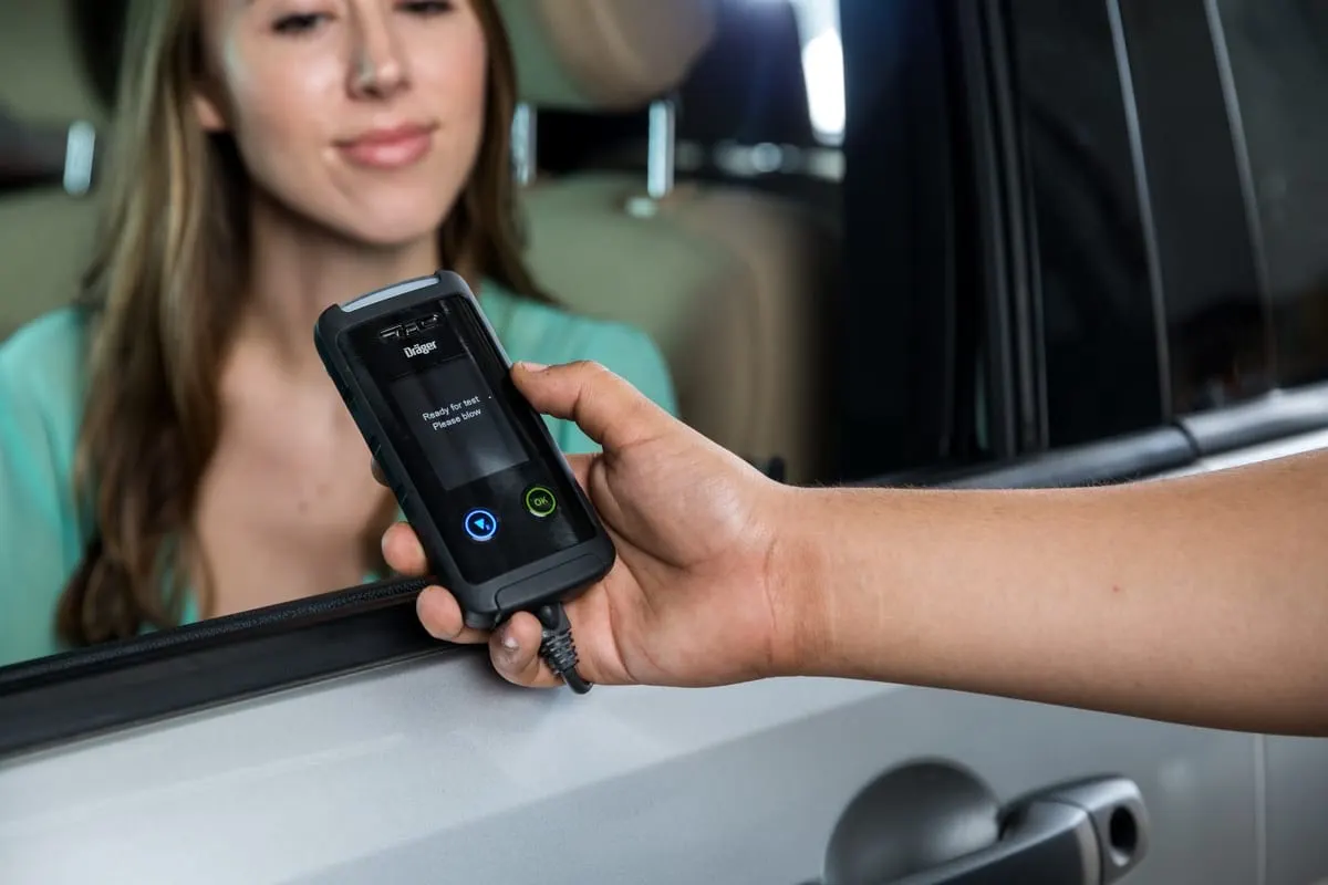 Hand holding a RoadGuard ignition interlock handset at a car window while the driver smiles.